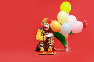 Photo of Happy clown with colorful balloons on red background, space for text