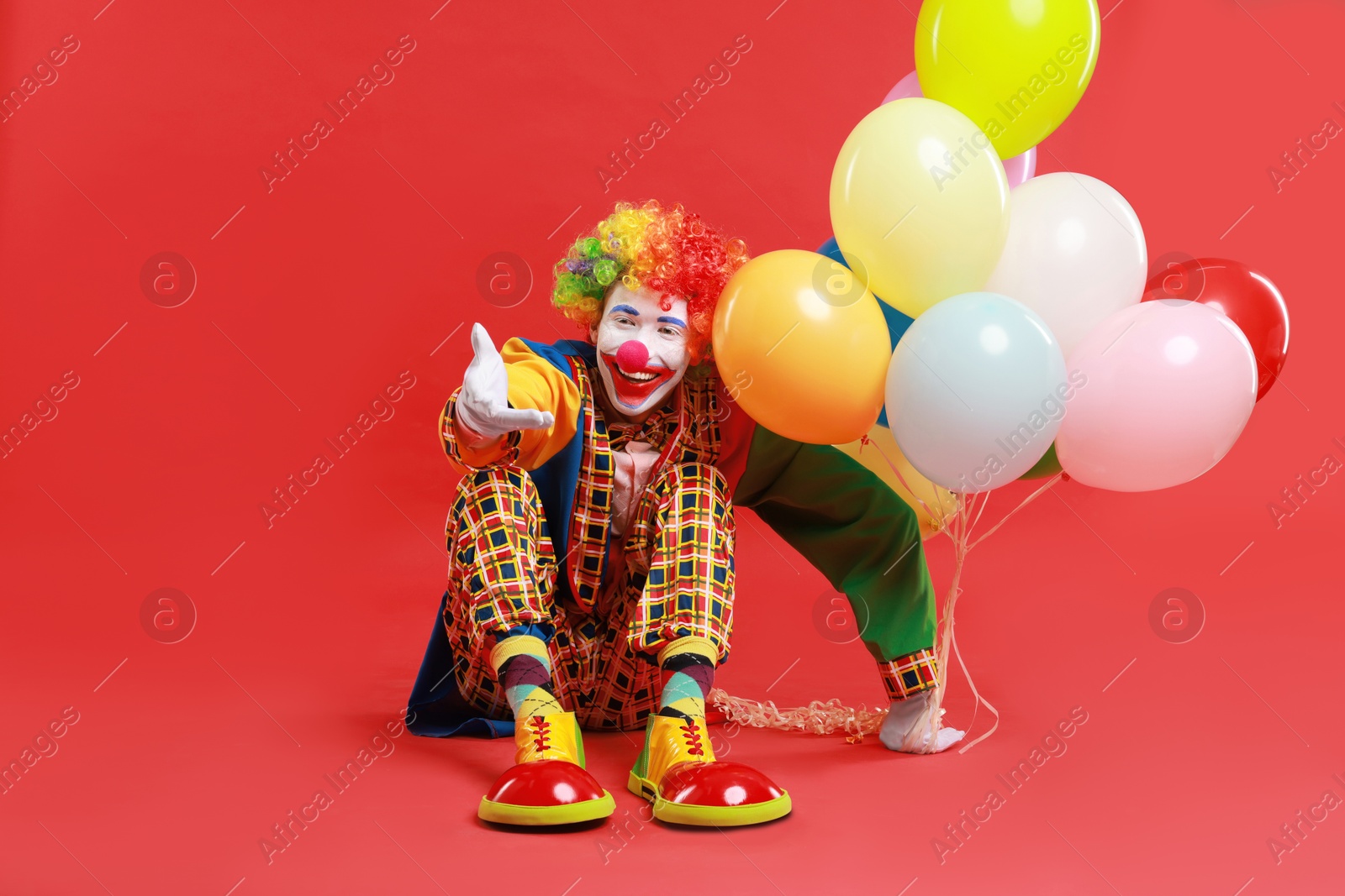 Photo of Happy clown with colorful balloons on red background, space for text