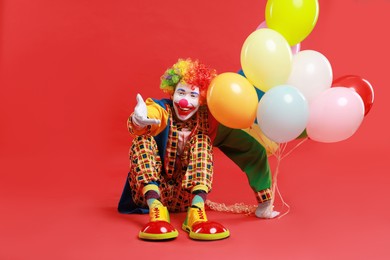 Photo of Happy clown with colorful balloons on red background, space for text