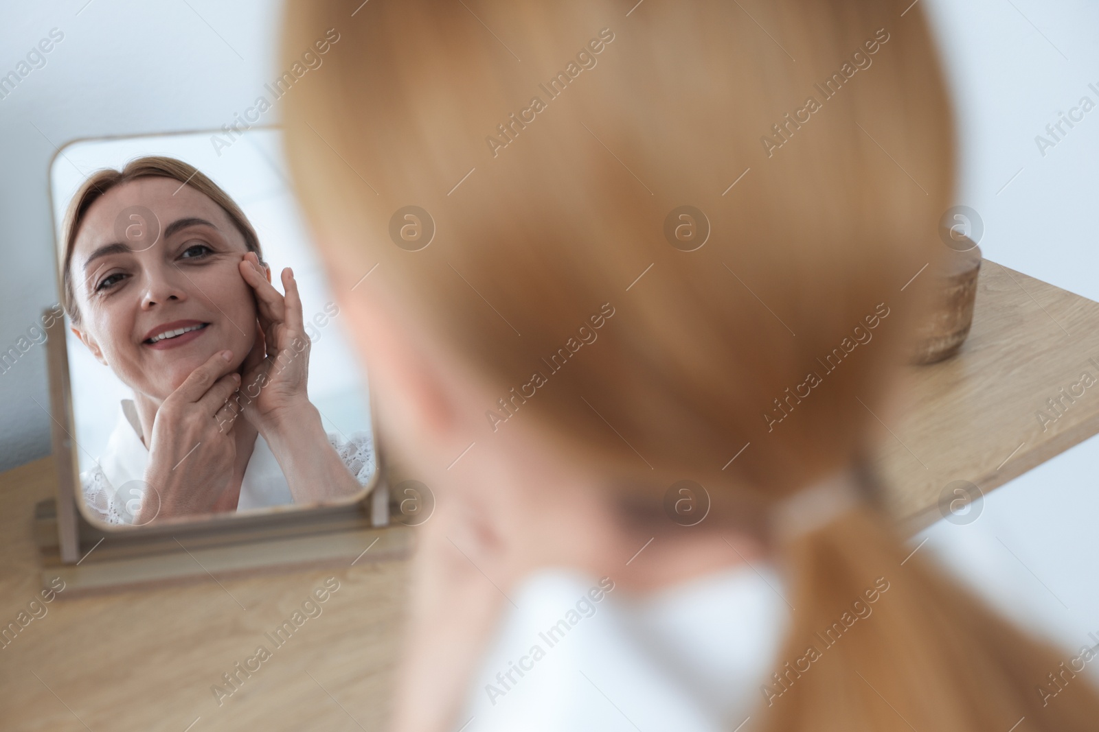 Photo of Smiling woman doing facial self massage near mirror at home