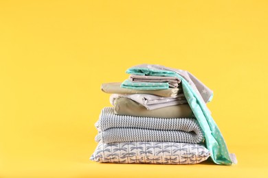 Photo of Stack of clean bed linen and pillow on yellow background. Space for text