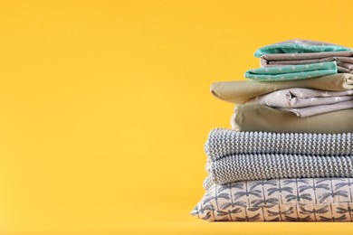 Photo of Stack of clean bed linen and pillow on yellow background. Space for text