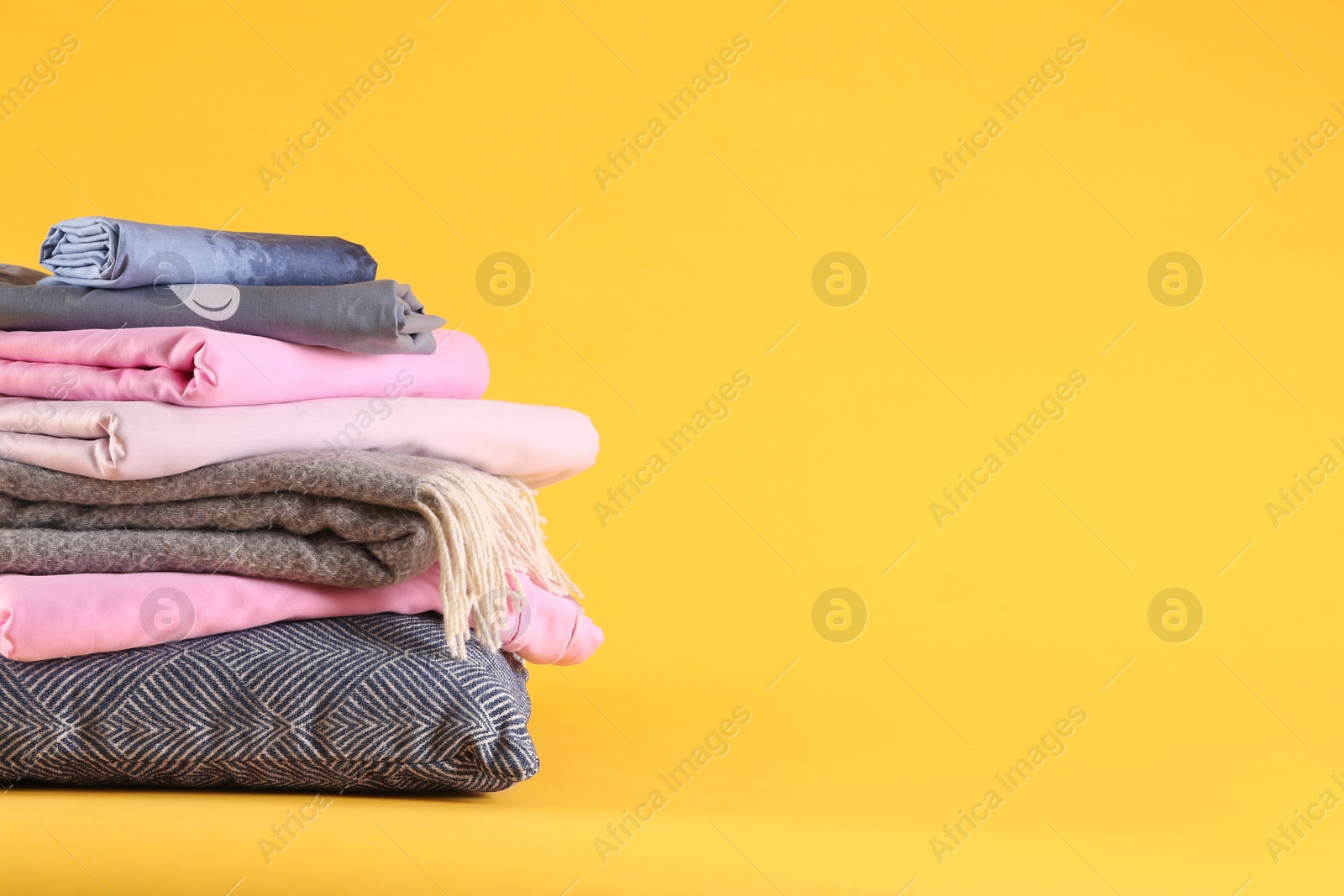 Photo of Stack of clean bed linen and pillow on yellow background. Space for text