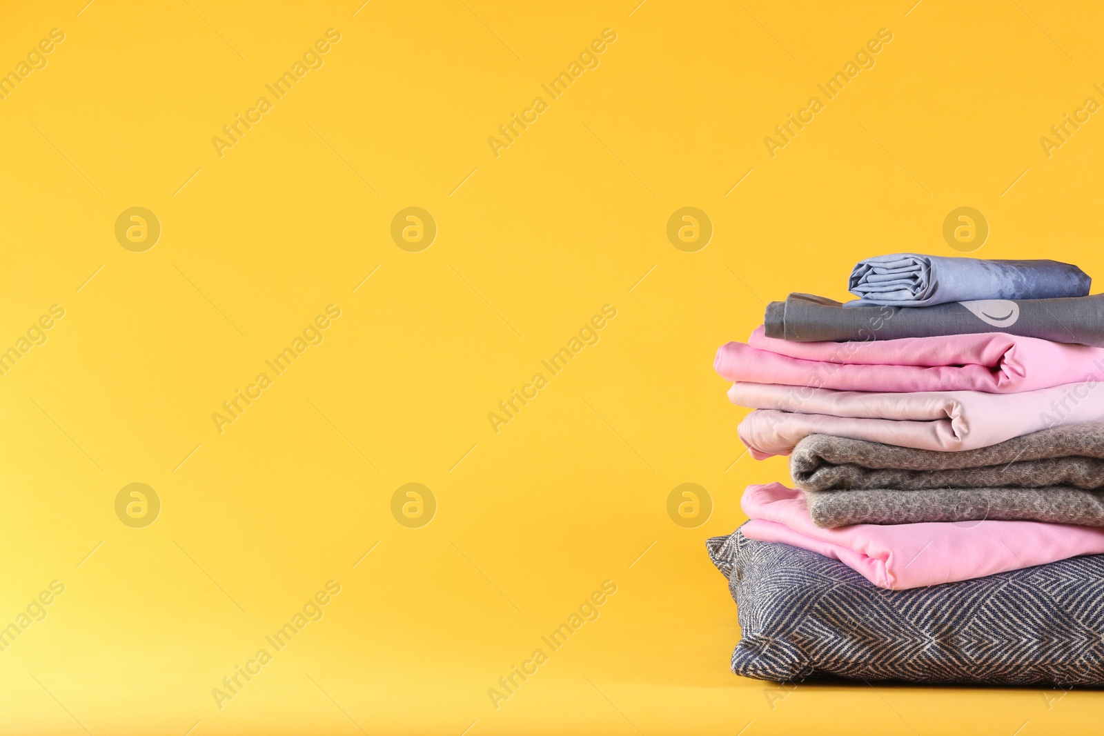 Photo of Stack of clean bed linen and pillow on yellow background. Space for text