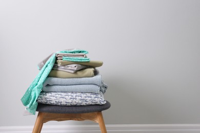 Stack of clean bed linen, plaid and pillow on stool near light grey wall. Space for text