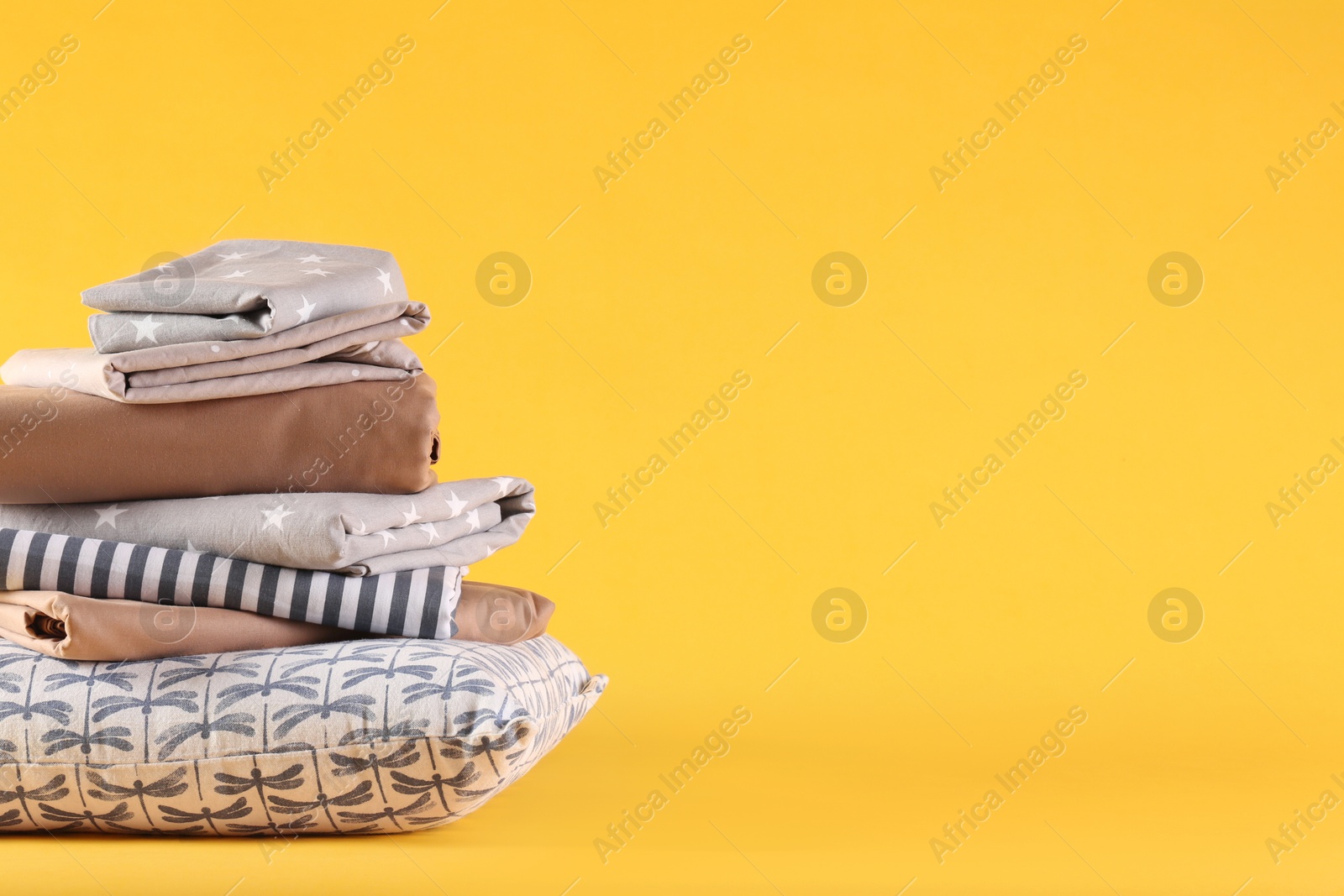 Photo of Stack of clean bed linen and pillow on yellow background. Space for text