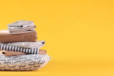 Photo of Stack of clean bed linen and pillow on yellow background. Space for text