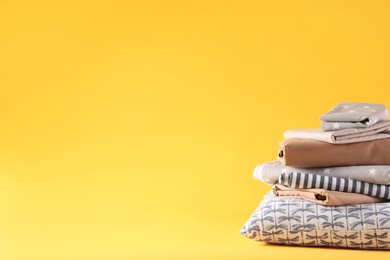 Photo of Stack of clean bed linen and pillow on yellow background. Space for text