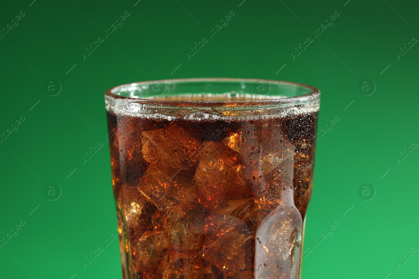 Photo of Glass of refreshing soda drink with ice cubes on green background, closeup