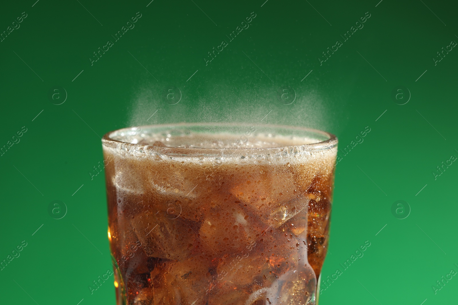 Photo of Glass of refreshing soda drink with ice cubes on green background, closeup