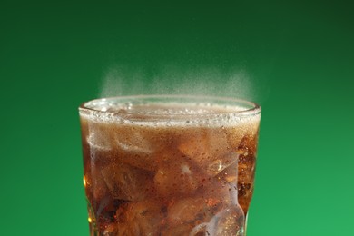 Glass of refreshing soda drink with ice cubes on green background, closeup