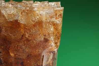 Photo of Glass of refreshing soda drink with ice cubes on green background, closeup. Space for text