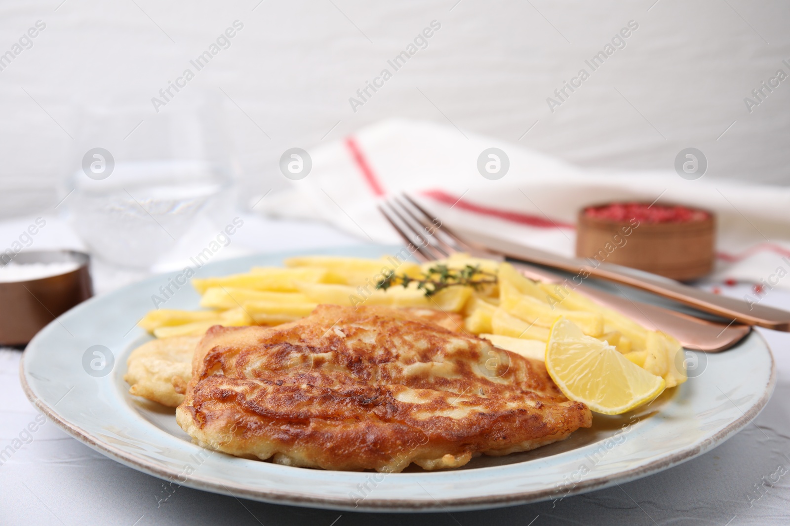 Photo of Tasty soda water battered fish, potato chips and lemon slice served on white textured table