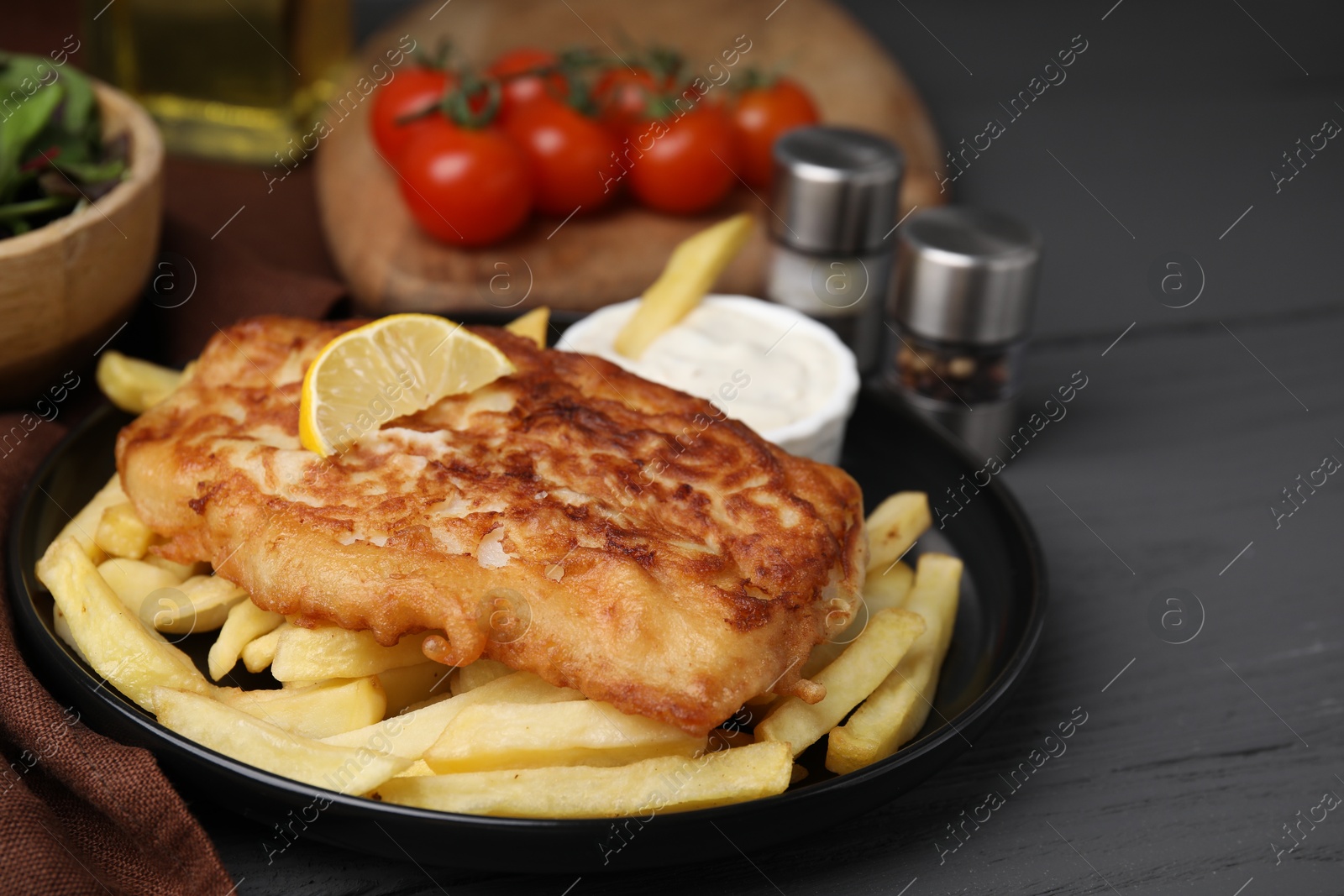 Photo of Tasty soda water battered fish, lemon slice and potato chips on dark wooden table