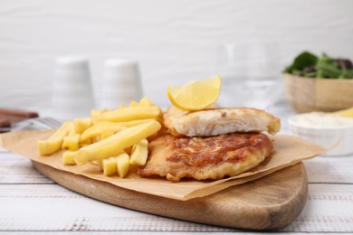 Photo of Tasty soda water battered fish, potato chips and lemon slice on white wooden table