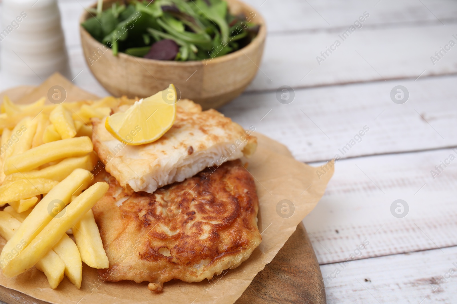 Photo of Tasty soda water battered fish, potato chips and lemon slice on white wooden table, space for text