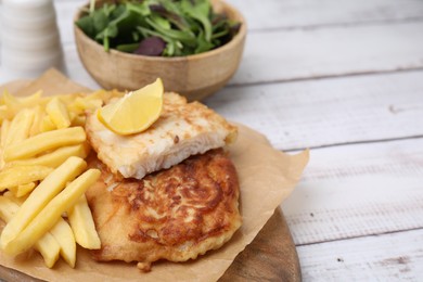 Photo of Tasty soda water battered fish, potato chips and lemon slice on white wooden table, space for text