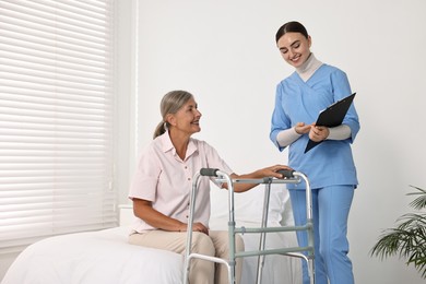 Photo of Nurse helping senior woman with walking frame in clinic