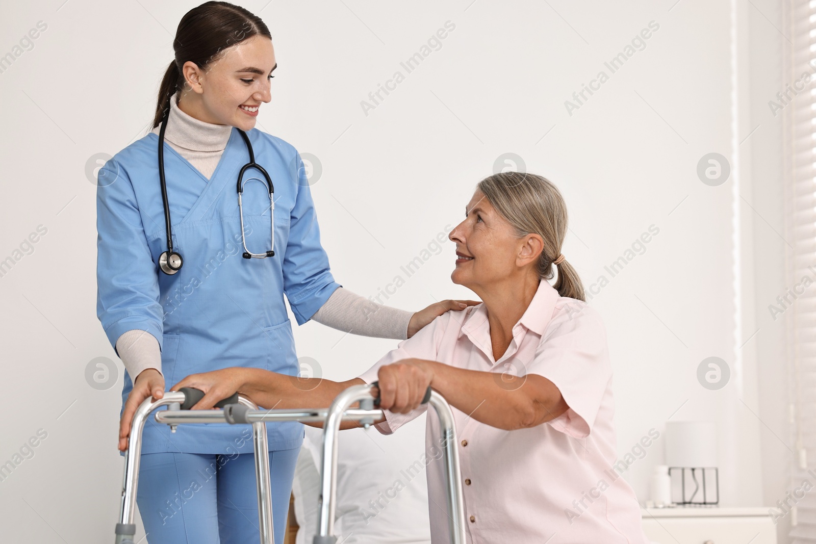 Photo of Nurse helping senior woman with walking frame in clinic