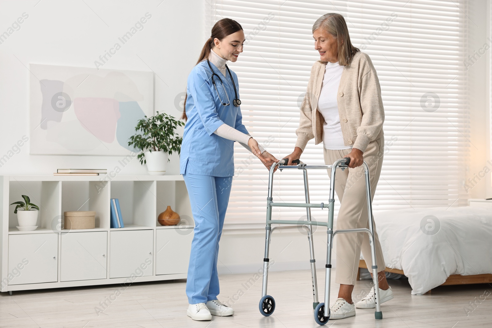 Photo of Nurse helping senior woman with walking frame in clinic