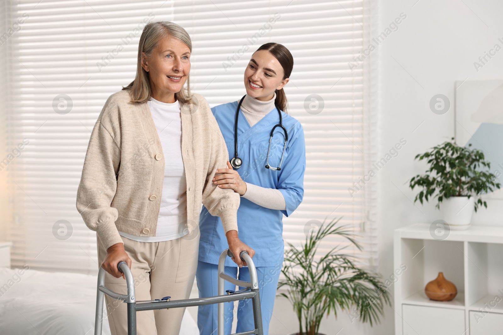 Photo of Nurse helping senior woman with walking frame in clinic