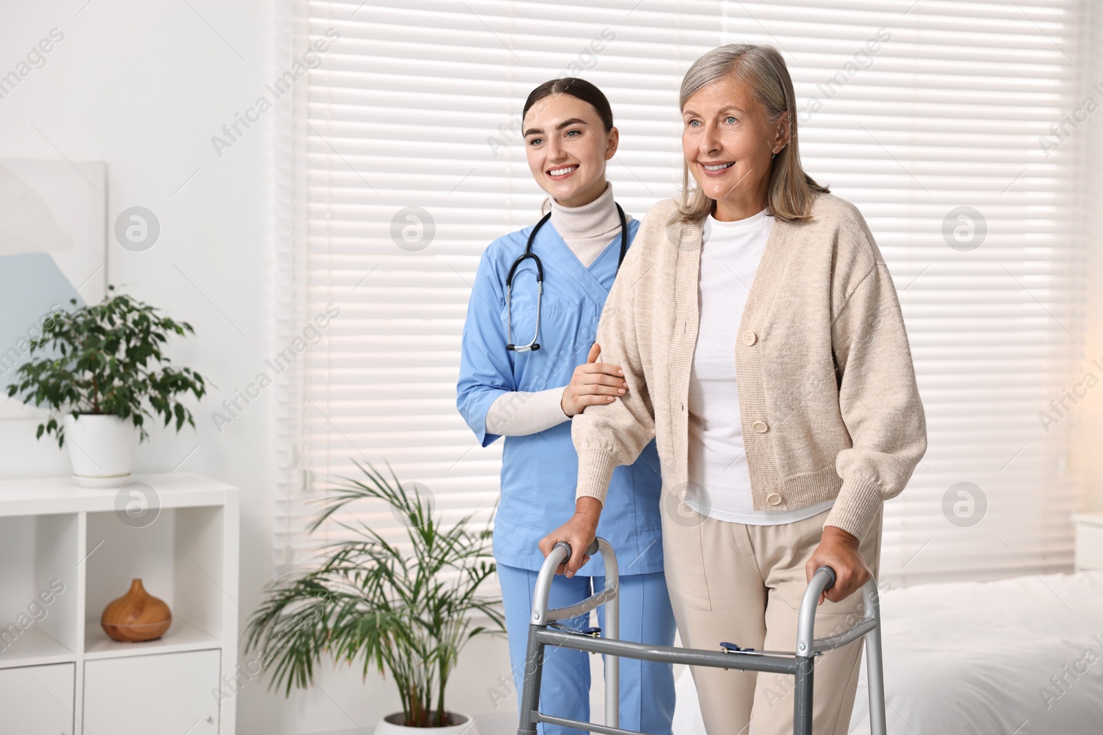 Photo of Nurse helping senior woman with walking frame in clinic