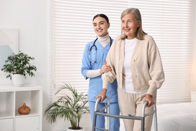 Photo of Nurse helping senior woman with walking frame in clinic