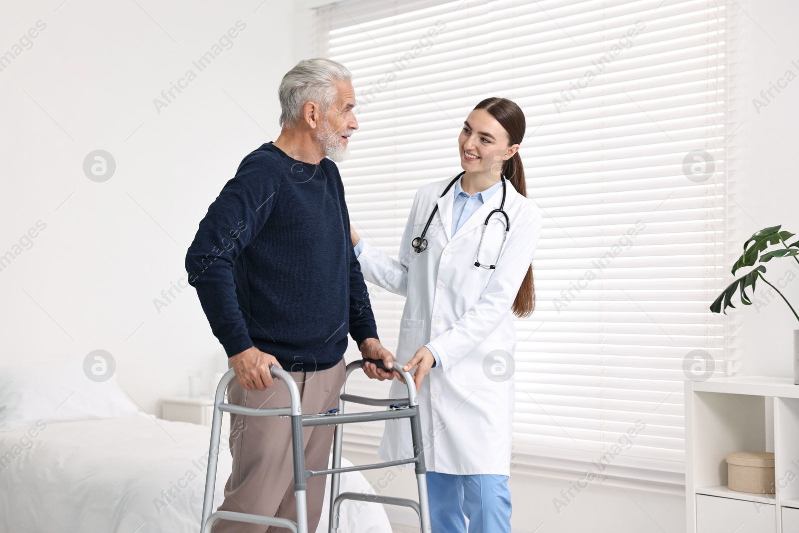 Photo of Doctor helping senior man with walking frame in clinic