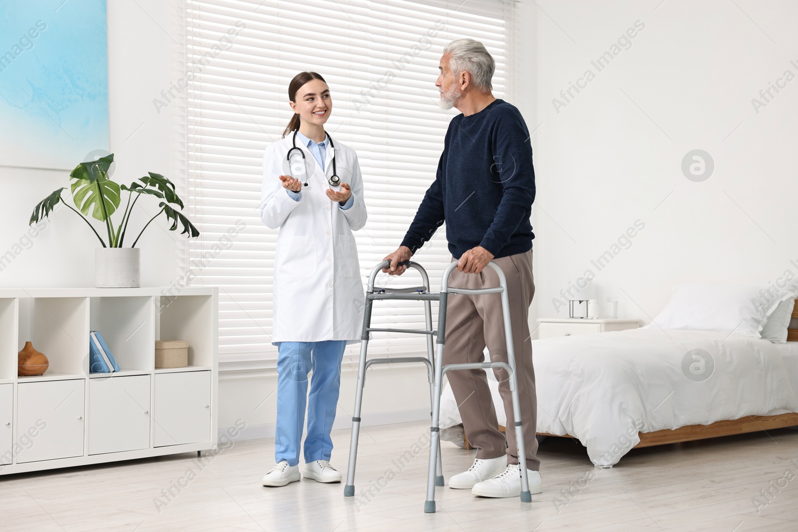 Photo of Doctor consulting senior patient with walking frame in hospital ward