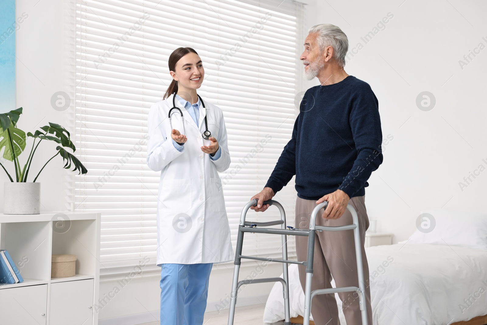 Photo of Doctor consulting senior patient with walking frame in hospital ward