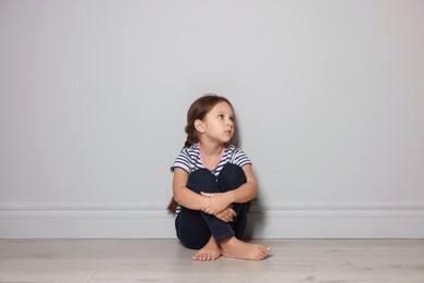 Orphanage concept. Sad girl sitting on floor indoors