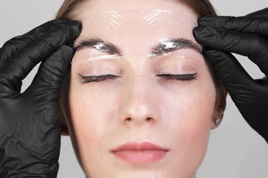 Photo of Brow lamination. Cosmetologist putting film onto woman's eyebrows against grey background, closeup