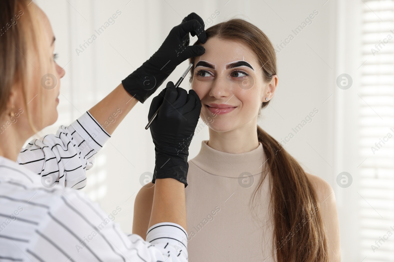 Photo of Beautician dyeing client’s eyebrows with henna in salon, closeup