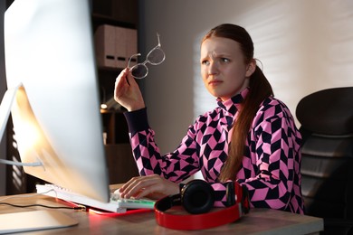 Photo of Girl looking at monitor at table with keyboard and headphones indoors