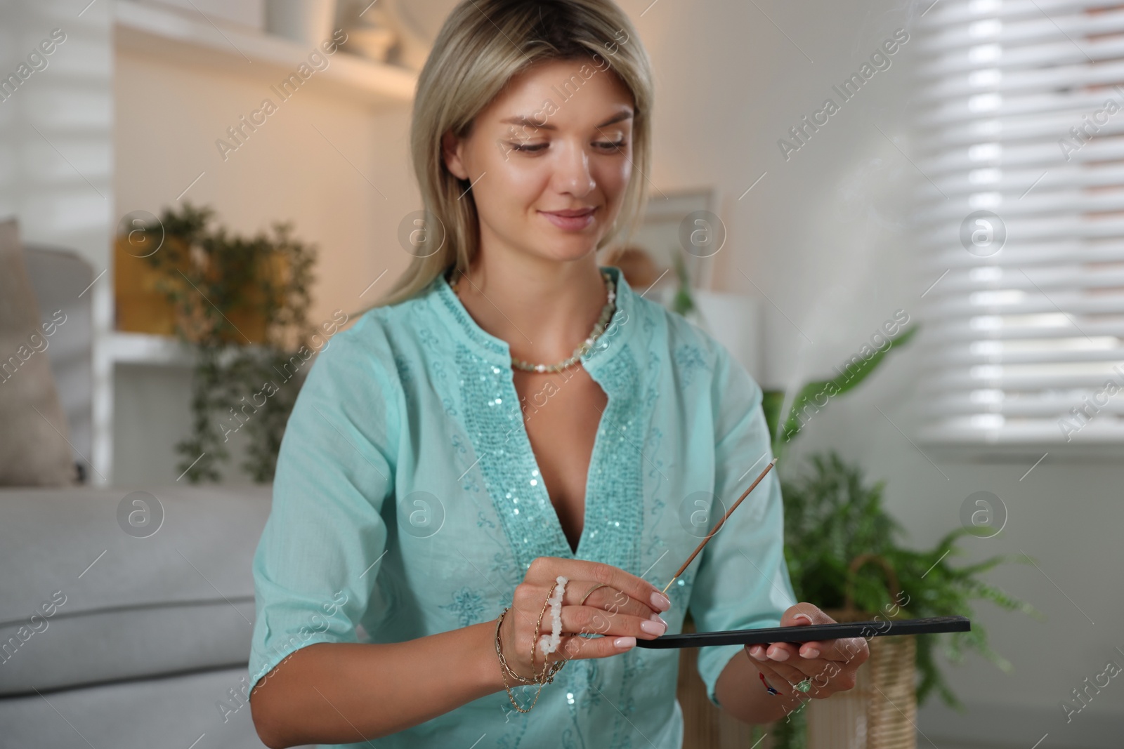 Photo of Beautiful young woman with incense stick smoldering in holder indoors