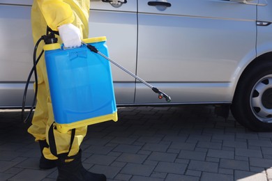 Pest control worker with spray tank near gray minibus outdoors, closeup