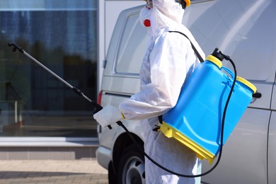 Photo of Pest control worker with spray tank near gray minibus outdoors, closeup