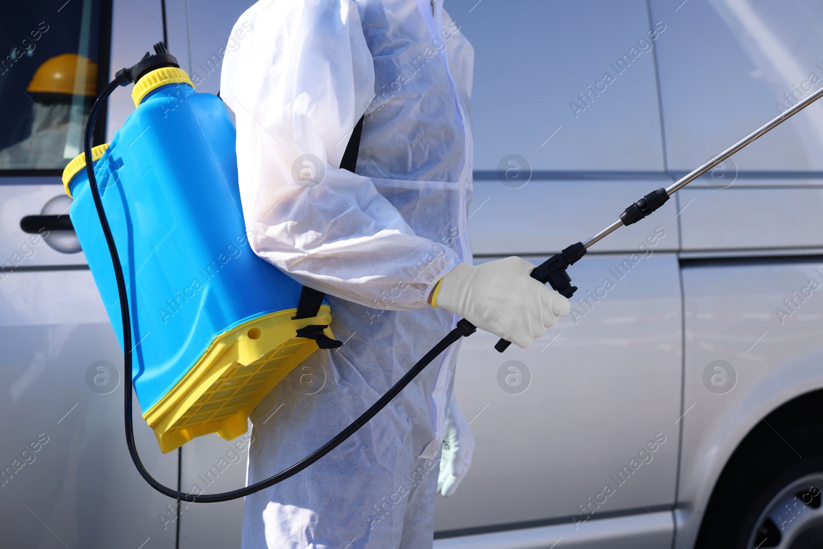 Photo of Pest control worker with spray tank near gray minibus outdoors, closeup