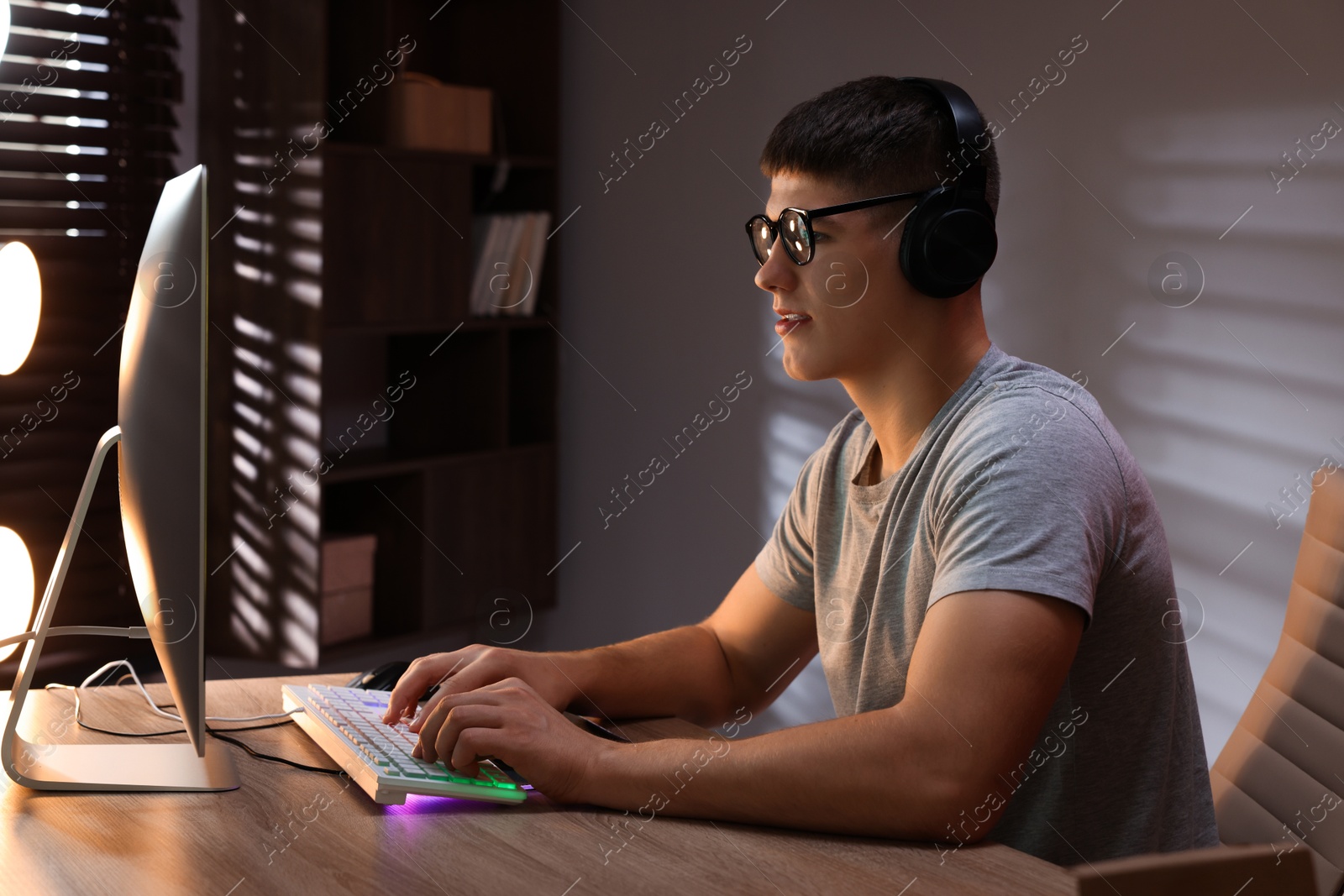 Photo of Young man playing video game with keyboard at wooden table indoors