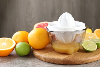 Photo of Plastic juicer and different citrus fruits on grey table, closeup