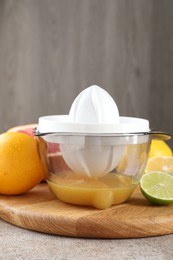 Plastic juicer and different citrus fruits on grey table