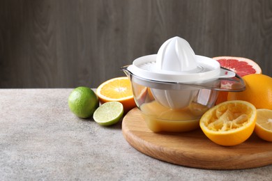 Photo of Plastic juicer and different citrus fruits on grey table. Space for text