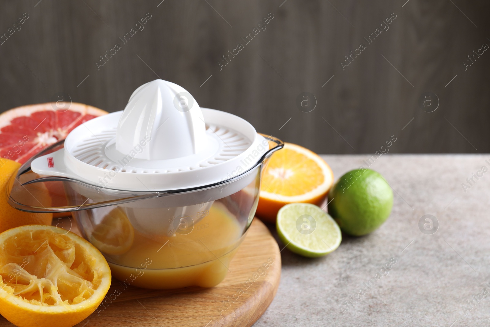 Photo of Plastic juicer and different citrus fruits on grey table, closeup. Space for text