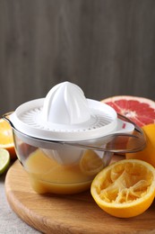 Plastic juicer and different citrus fruits on table, closeup