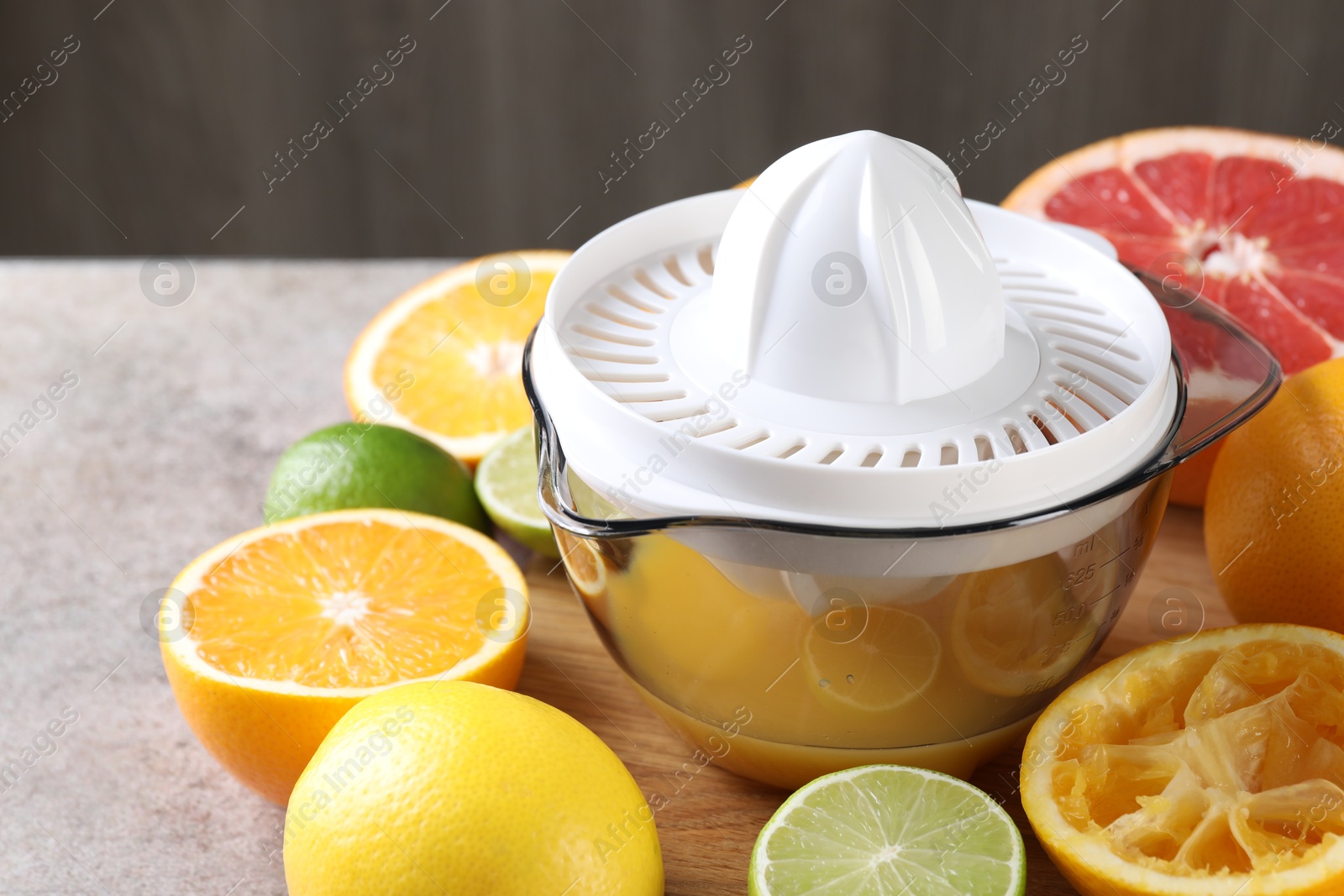 Photo of Plastic juicer and different citrus fruits on grey table, closeup