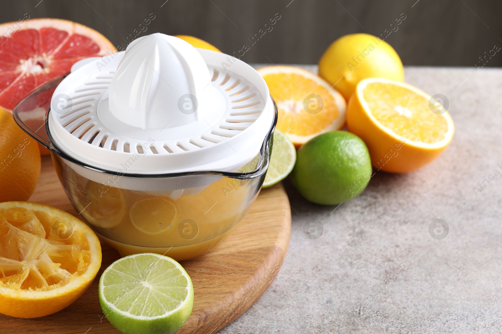 Photo of Plastic juicer and different citrus fruits on grey table, closeup