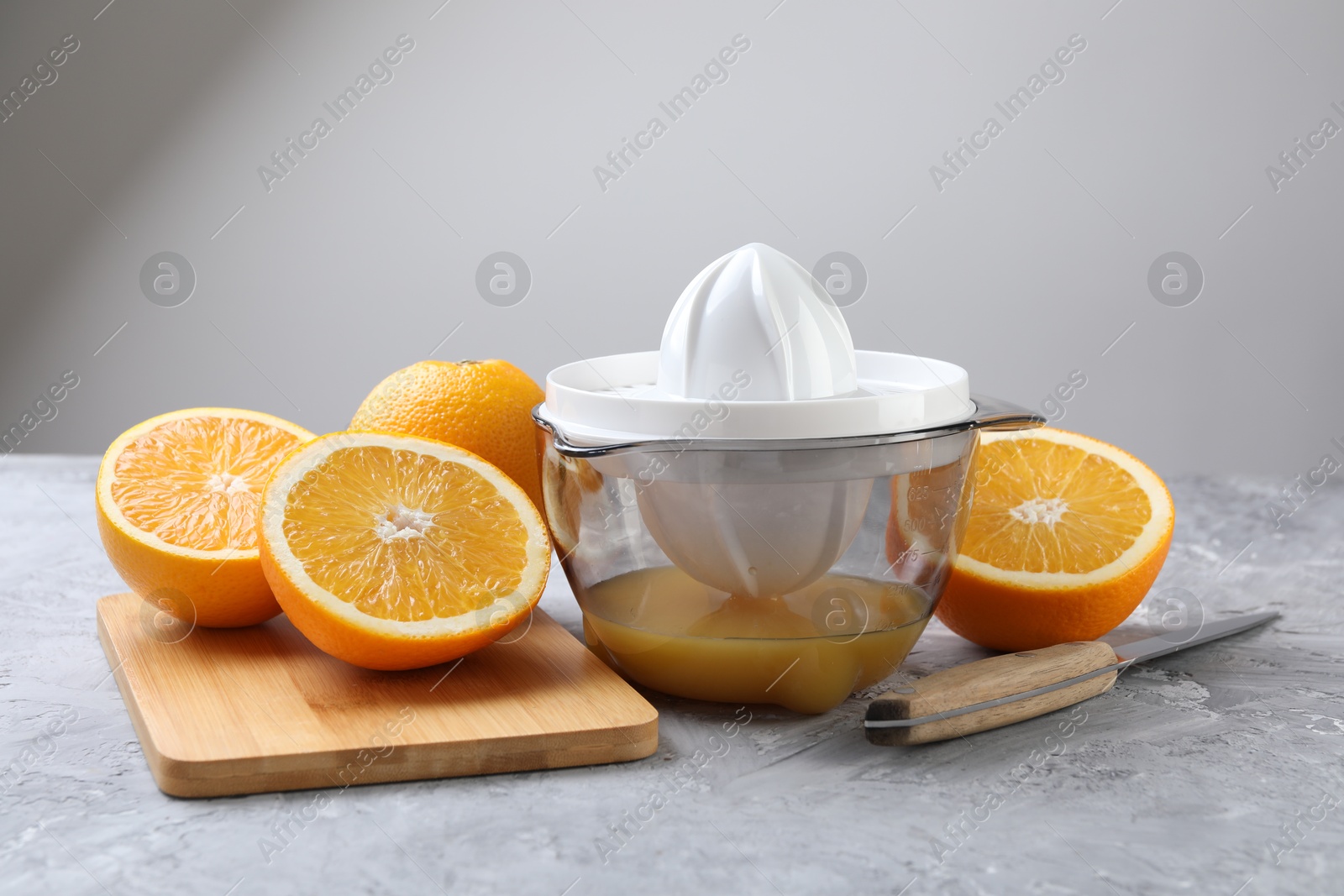 Photo of Plastic juicer, oranges and knife on grey table