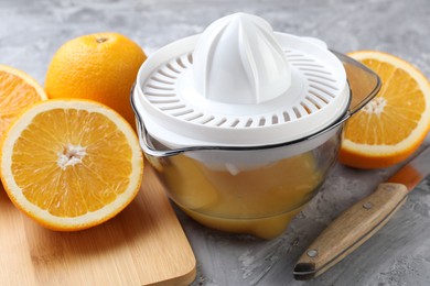 Photo of Plastic juicer, oranges and knife on grey table, closeup