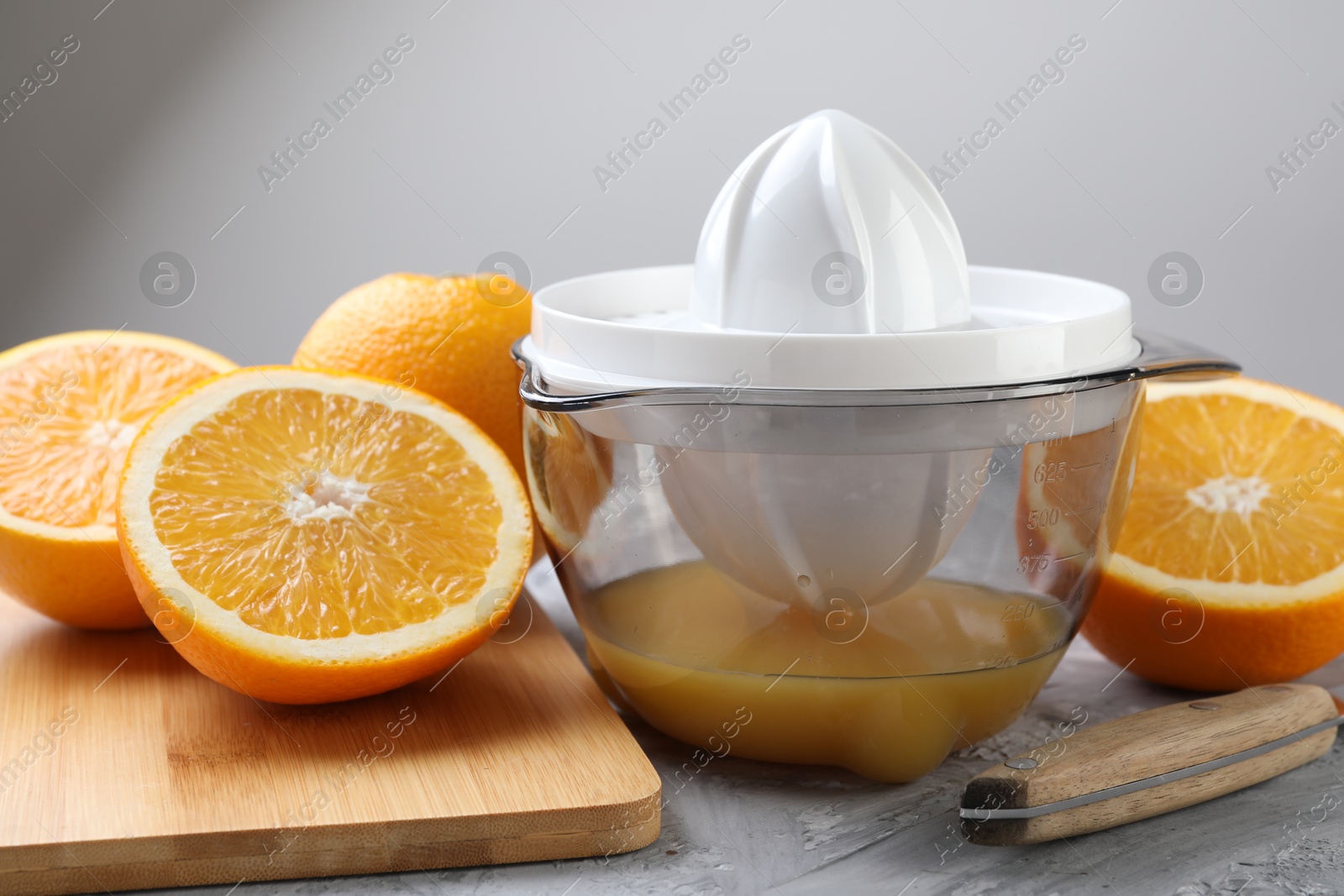 Photo of Plastic juicer, oranges and knife on grey table, closeup