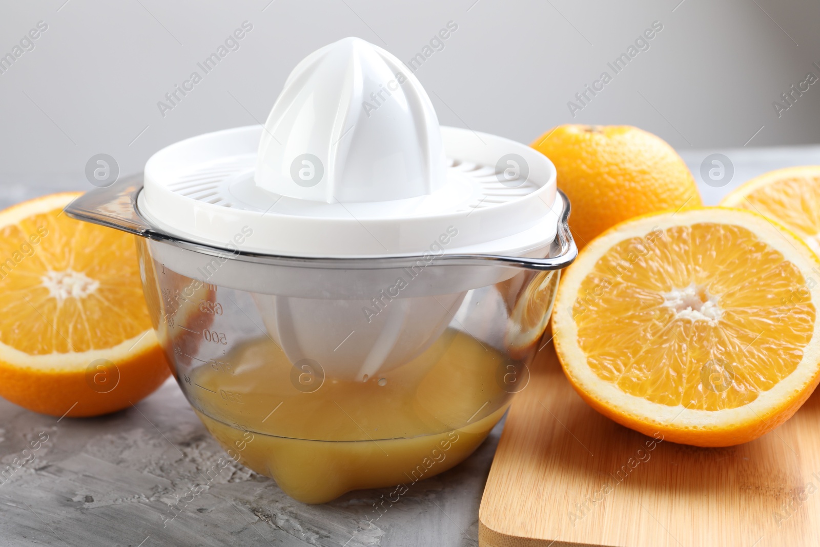 Photo of Plastic juicer and oranges on grey table, closeup